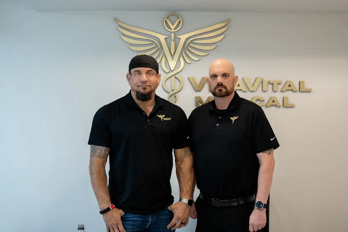 Two VidaVital Medical team members in front of the clinic logo wall